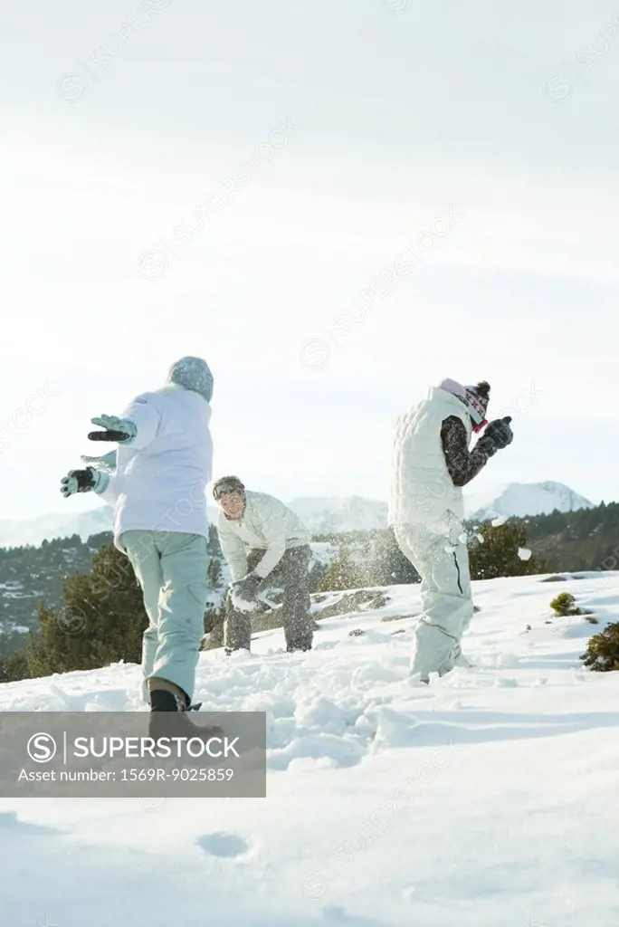Young friends throwing snowballs at each other, full length