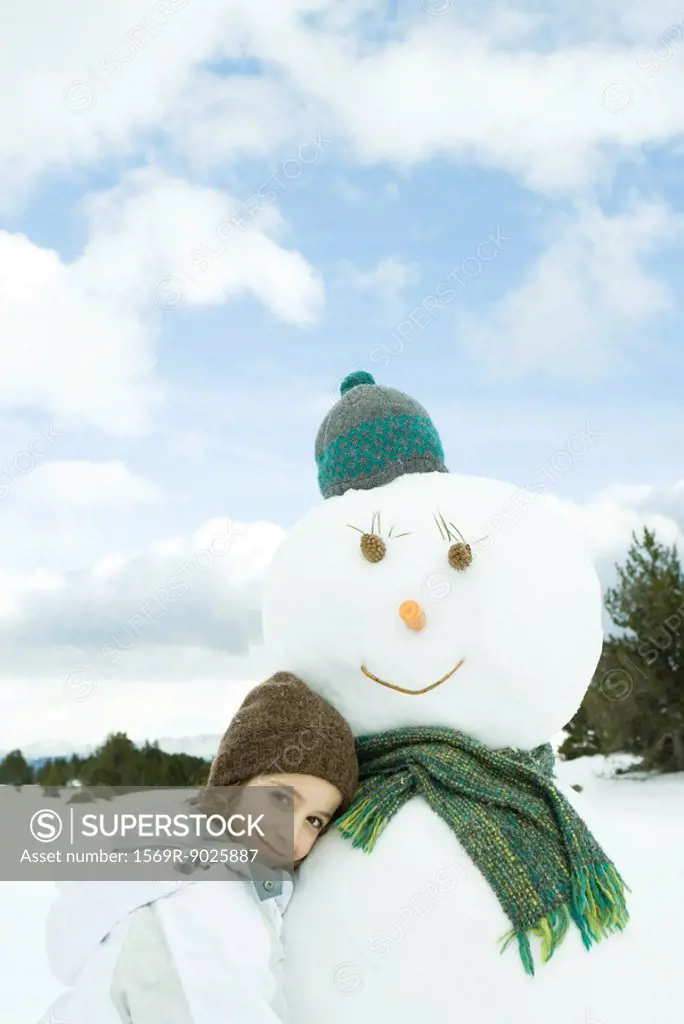 Girl leaning against snowman, smiling at camera, portrait