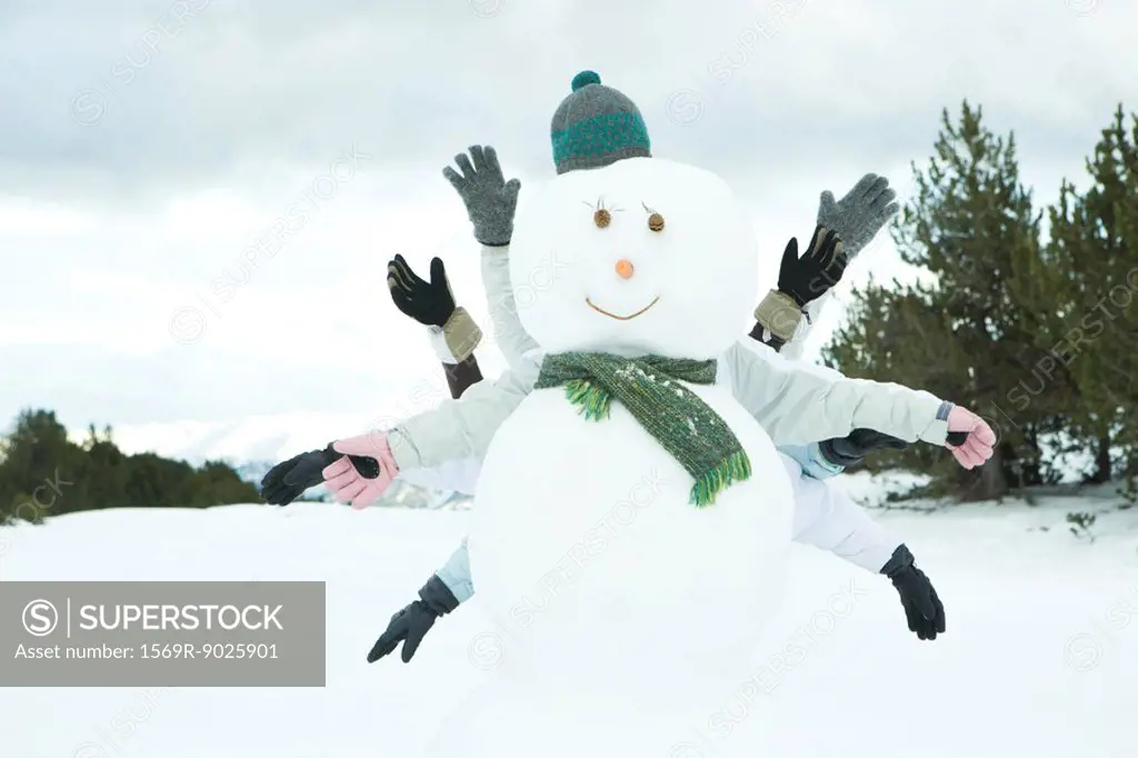 Young friends hiding behind snowman, arms out