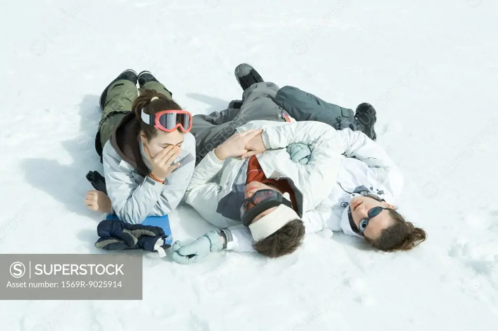 Three young friends reclining in snow, one holding head