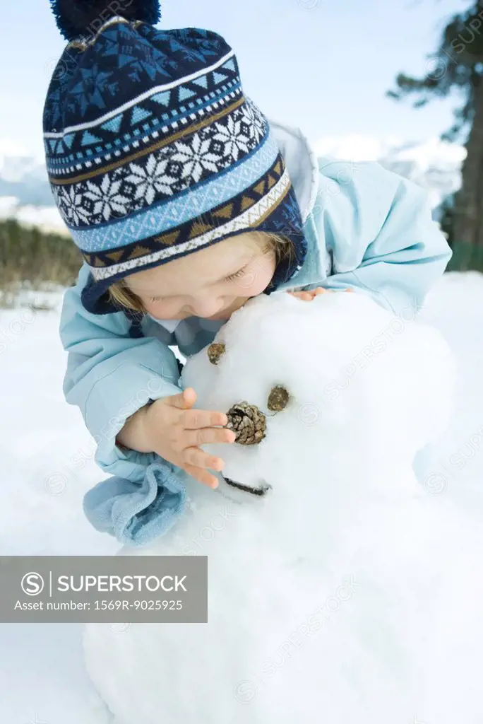 Toddler girl building snowman, bending over