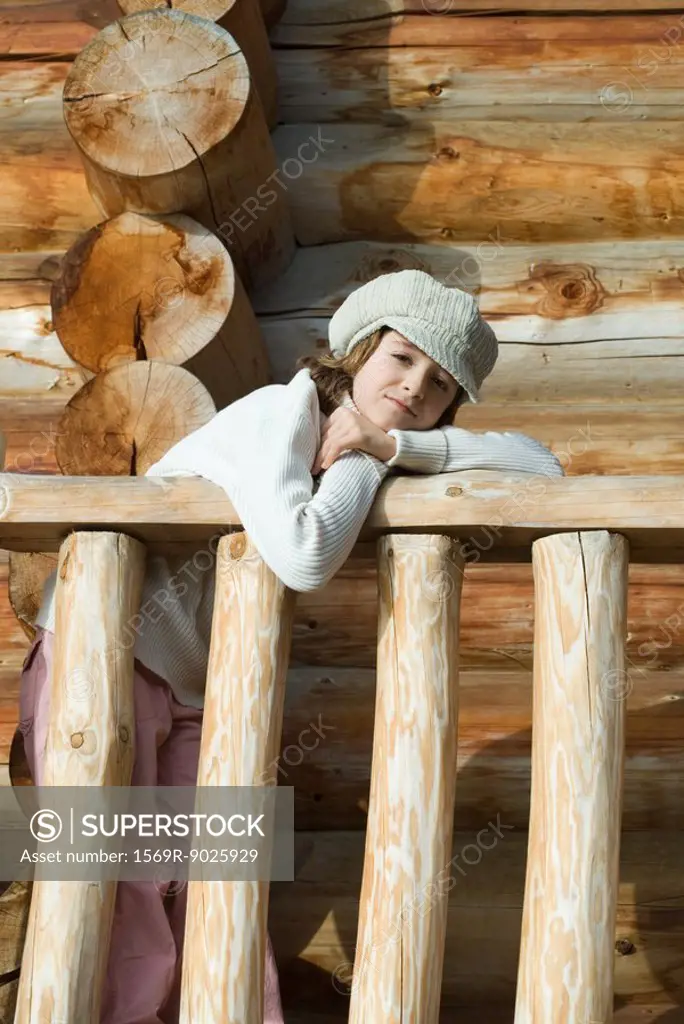 Girl leaning on railing of log cabin, looking at camera