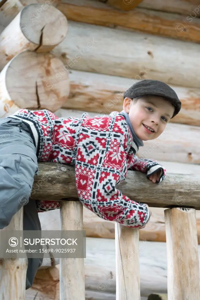 Boy climbing on rail in front of log cabin, smiling at camera