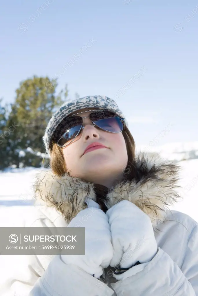 Teenage girl wearing parka and sunglasses in snow, head back, portrait