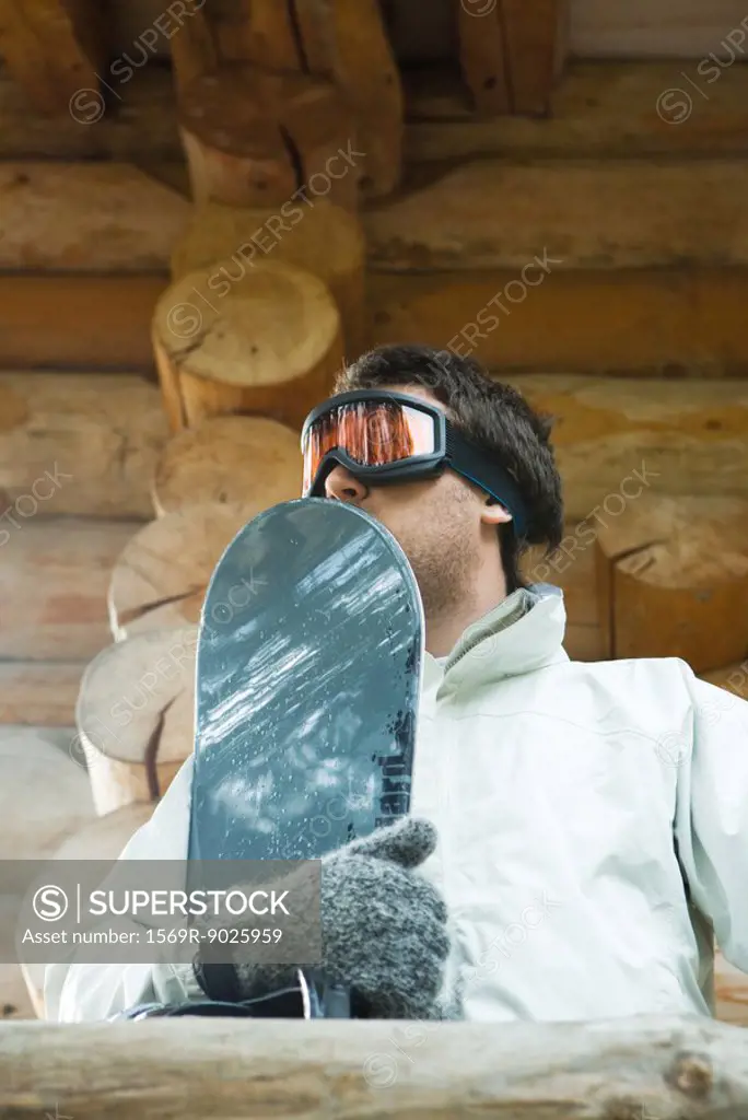 Young man holding snowboard, low angle view