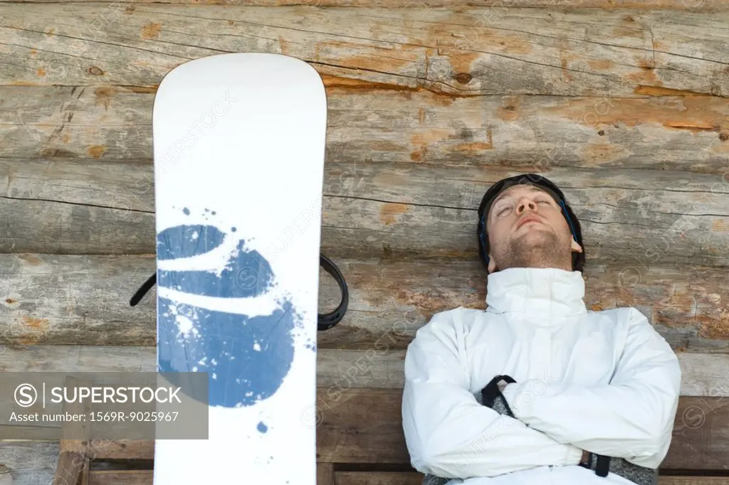 Young man sitting on bench next to snowboard, napping