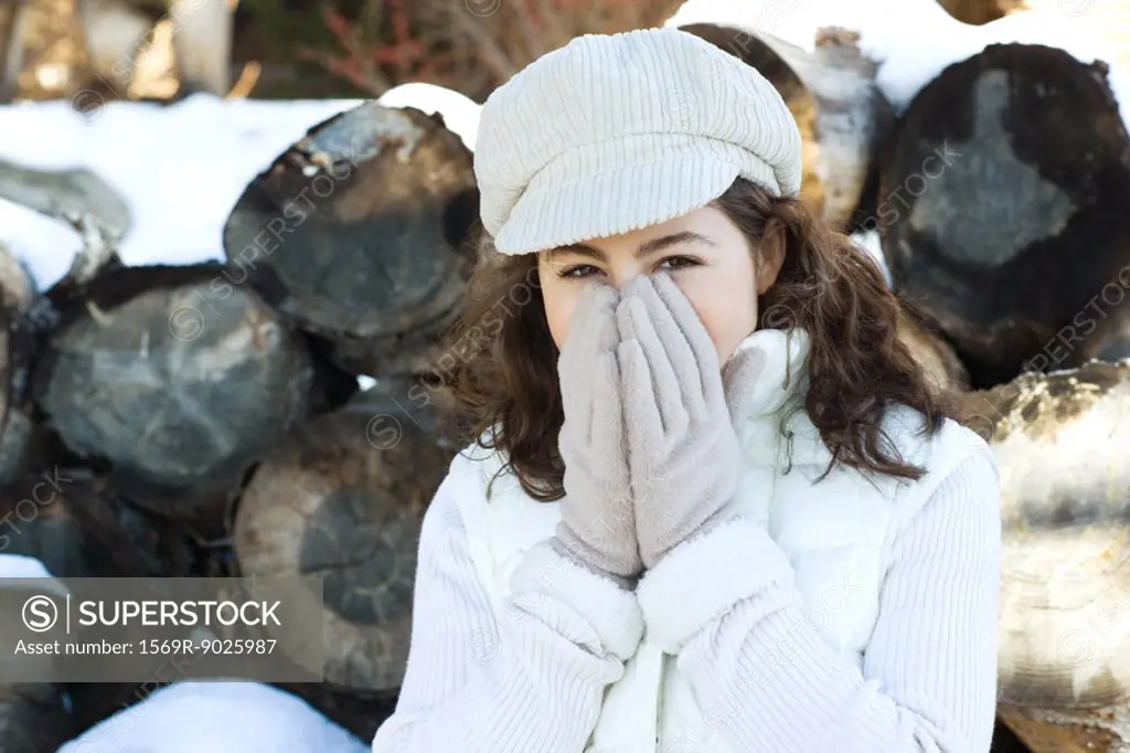 Teenage girl covering face with hands, in front of stack of timber