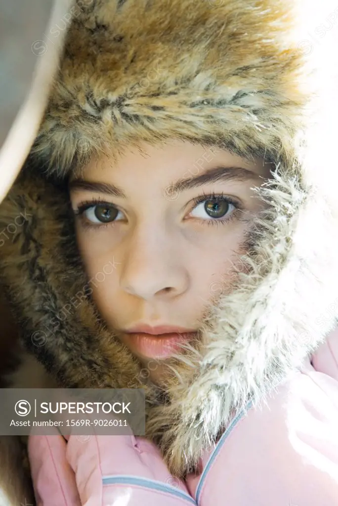 Preteen girl, wearing fur hat, holding flaps together over neck, close-up portrait