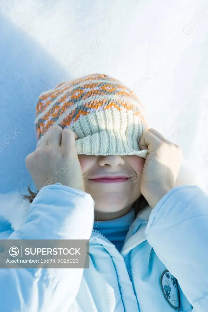 Girl lying on snow, pulling hat over eyes