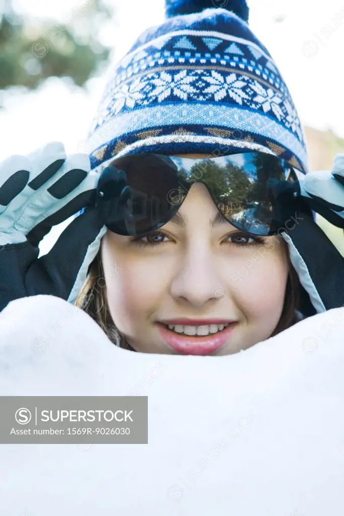 Teenage girl in snow, wearing winter clothes, lifting sunglasses, portrait