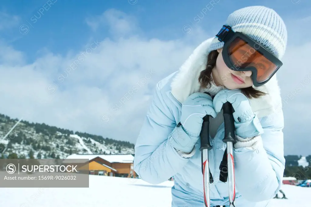 Teen girl leaning on ski sticks, in snowy landscape, portrait