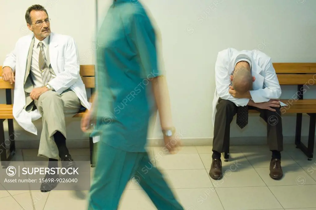 Doctors sitting in hospital corridor, one with head down