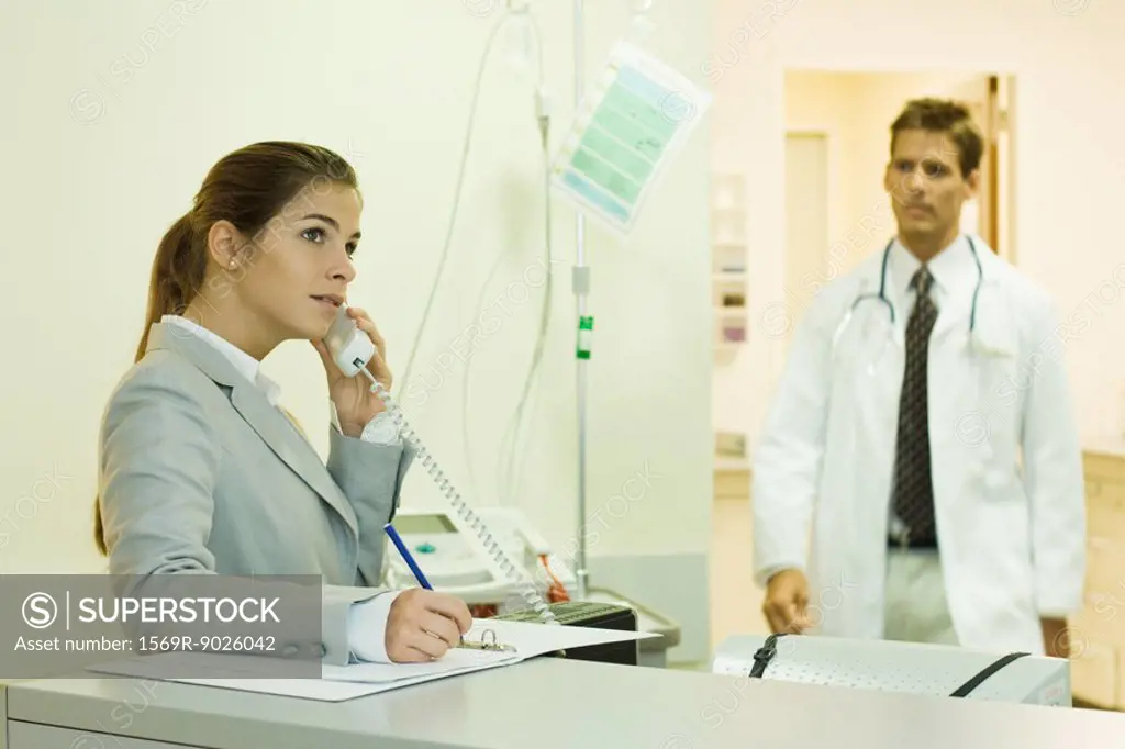 Woman using phone in doctor´s office, doctor approaching in background