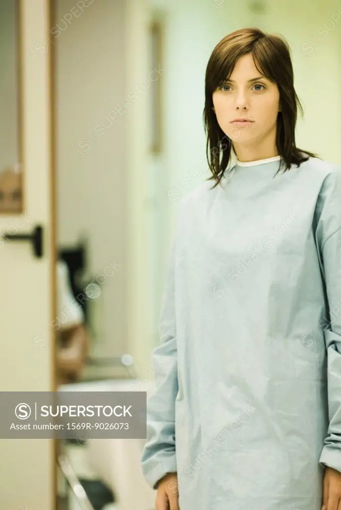Young woman wearing hospital gown, looking away, hospital corridor in background