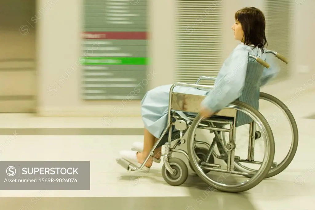 Female patient using wheelchair in hospital corridor, blurred motion