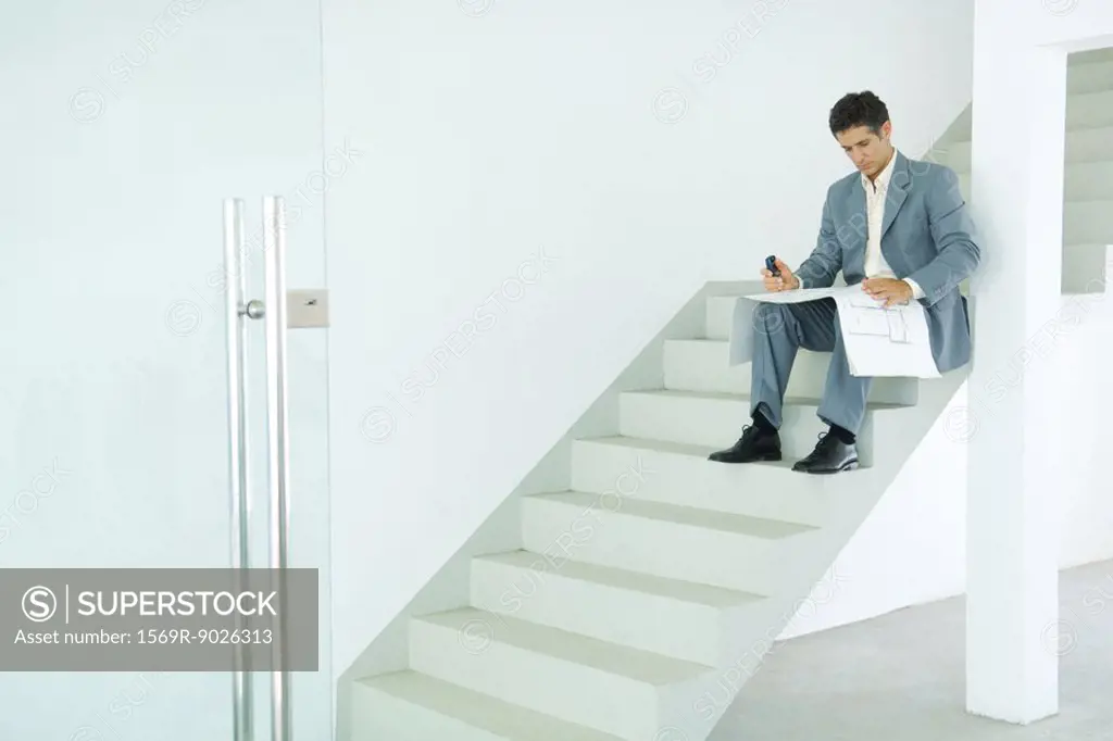 Man sitting on stairs, looking at blueprints