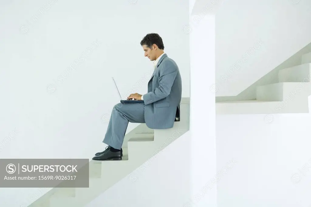 Man sitting on stairs, using laptop