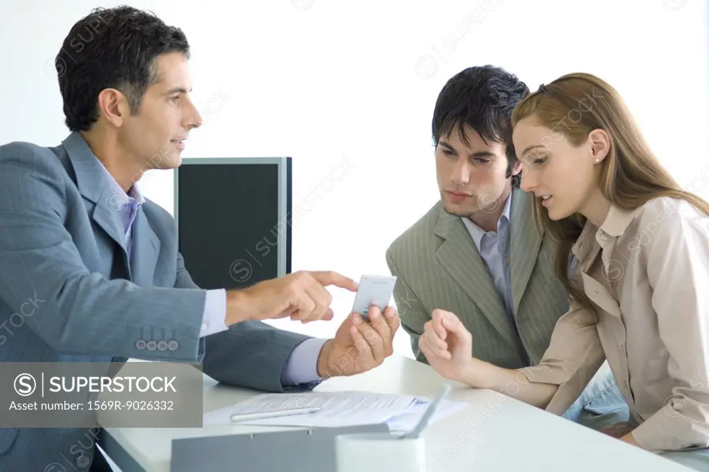 Man in suit sitting across from young couple, pointing to calculator