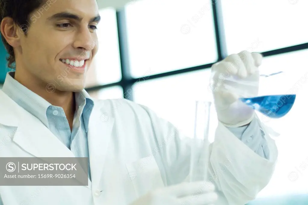 Male scientist transfering liquid from flask to cylinder, smiling