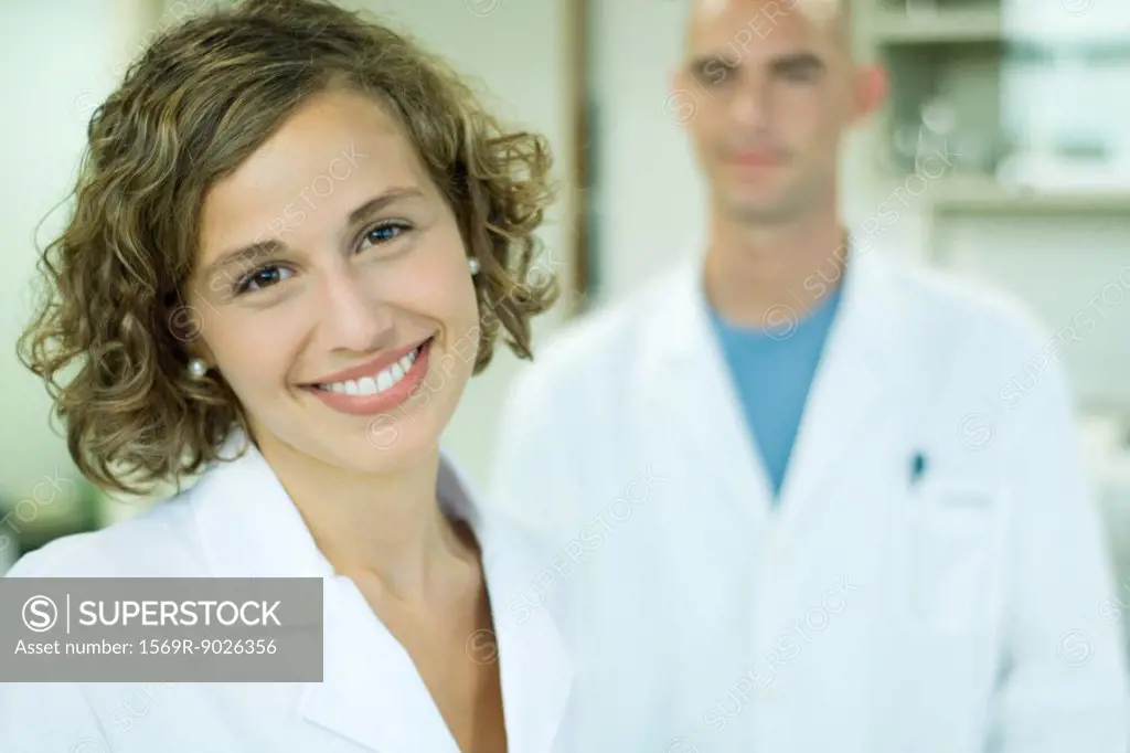 Female doctor smiling, male colleague in background, portrait
