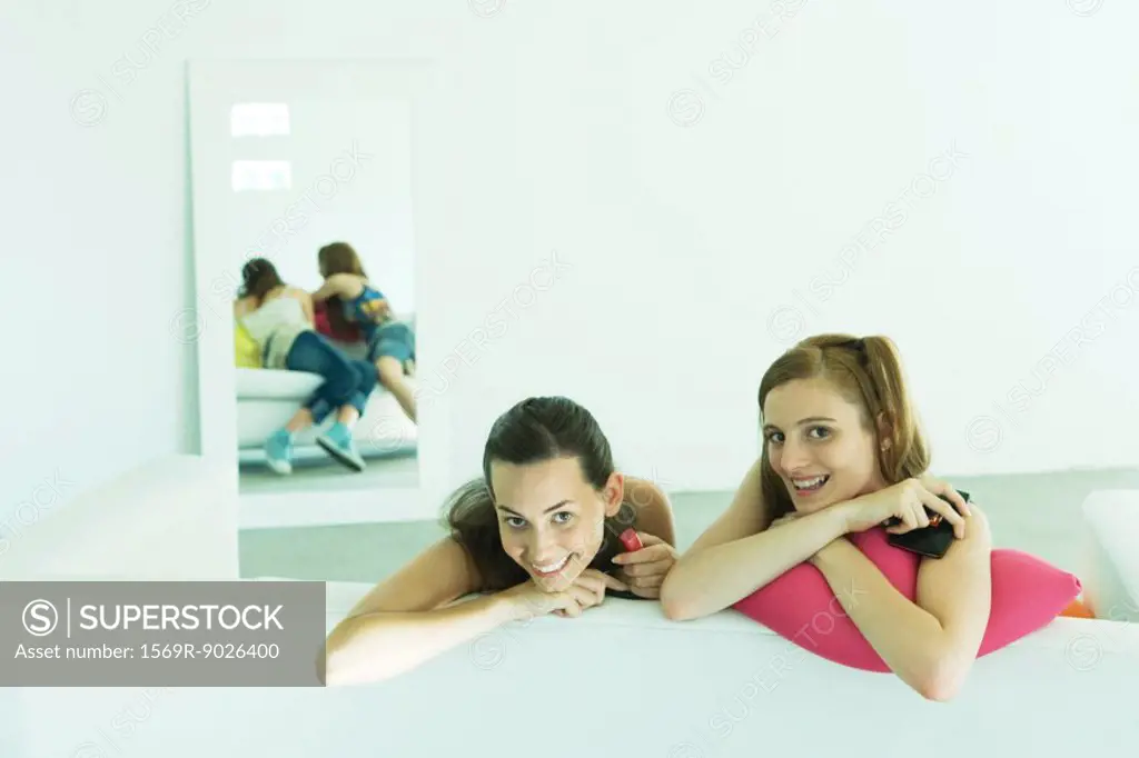 Two young friends leaning over back of couch, smiling at camera