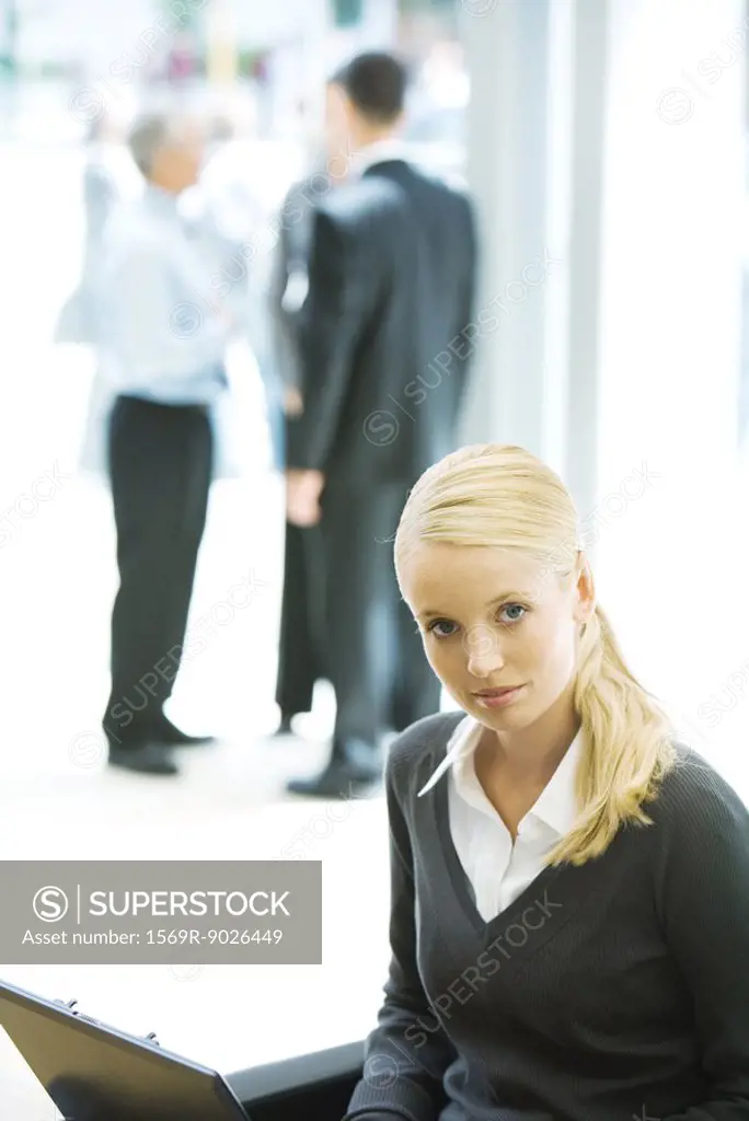 Young businesswoman using laptop, looking at camera, associates in background