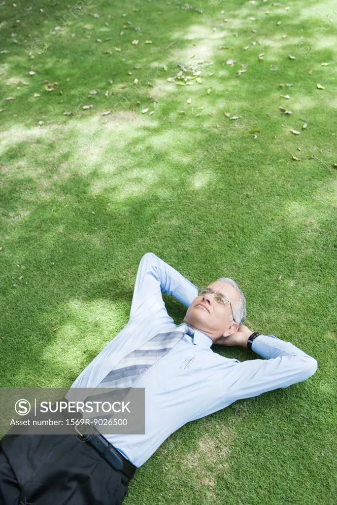 Businessman lying on grass with hands behind head