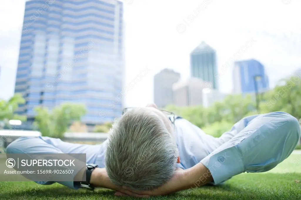 Businessman lying on grass, hands behind head