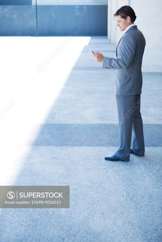 Businessman looking down at cell phone, full length