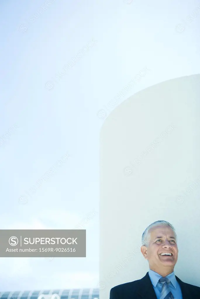 Businessman laughing, head and shoulders, cylinder and sky in background