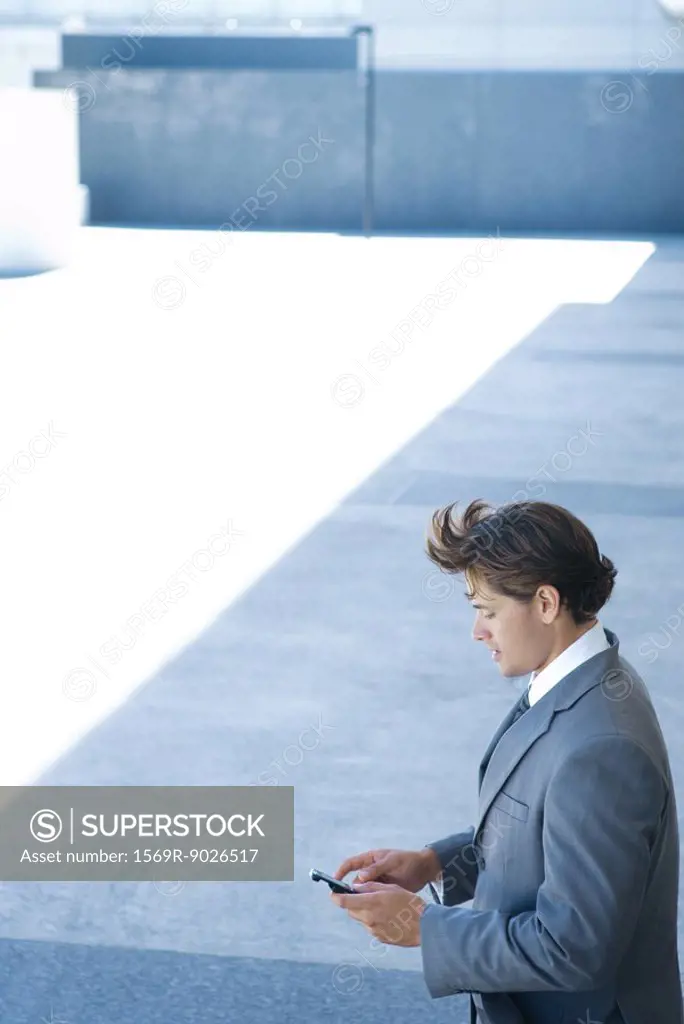 Businessman standing outdoors looking down at cell phone, high angle view
