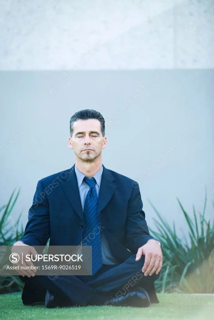 Businessman sitting cross-legged on grass, eyes closed