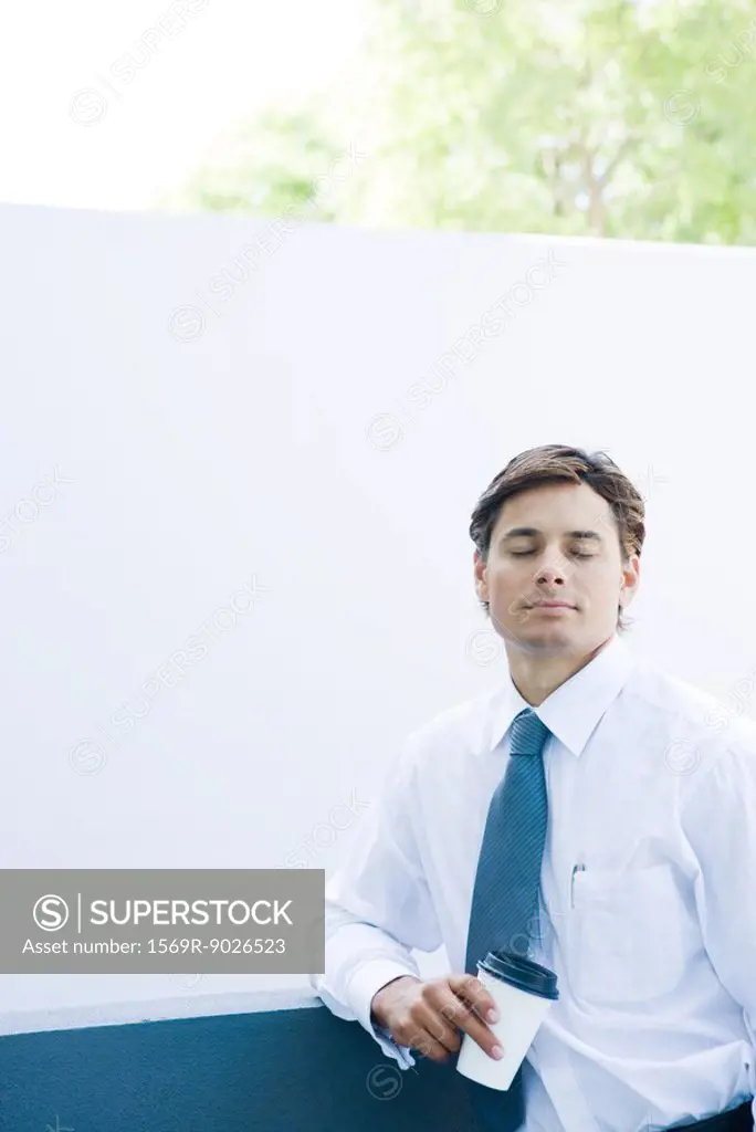 Businessman holding coffee cup, eyes closed