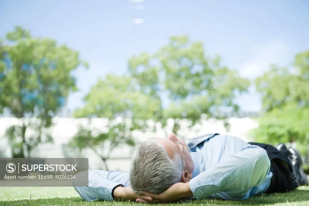 Businessman lying on grass, hands behind head