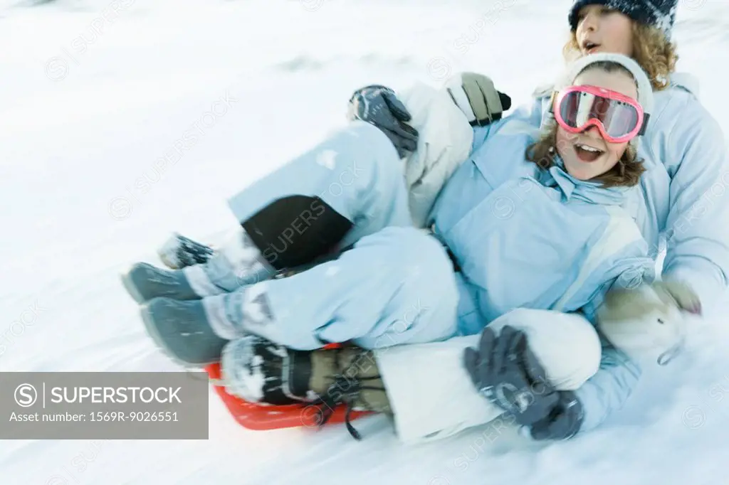 Two young friends riding sled together, blurred motion