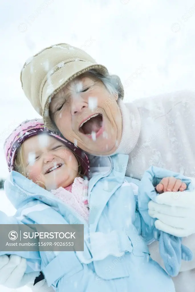 Senior woman and granddaughter cheek to cheek in snow, smiling, eyes, closed