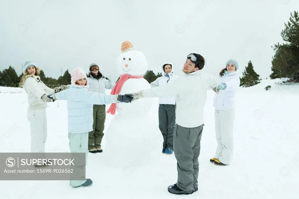 Young friends standing in circle around snowman, holding hands, smiling at camera