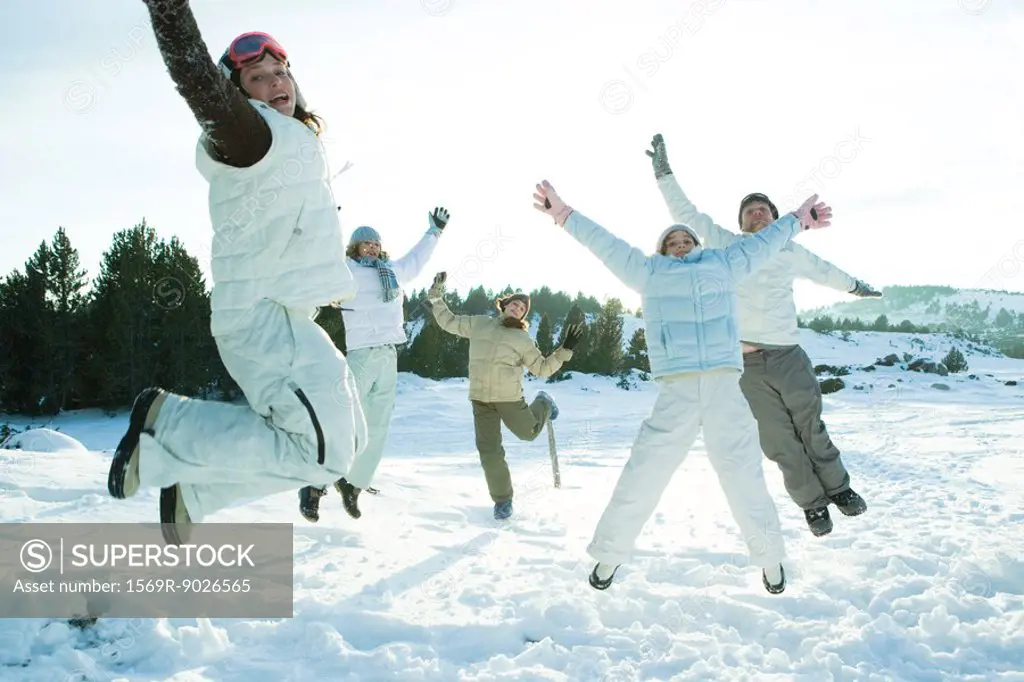 Young friends jumping in the air, dressed in winter clothing, smiling at camera