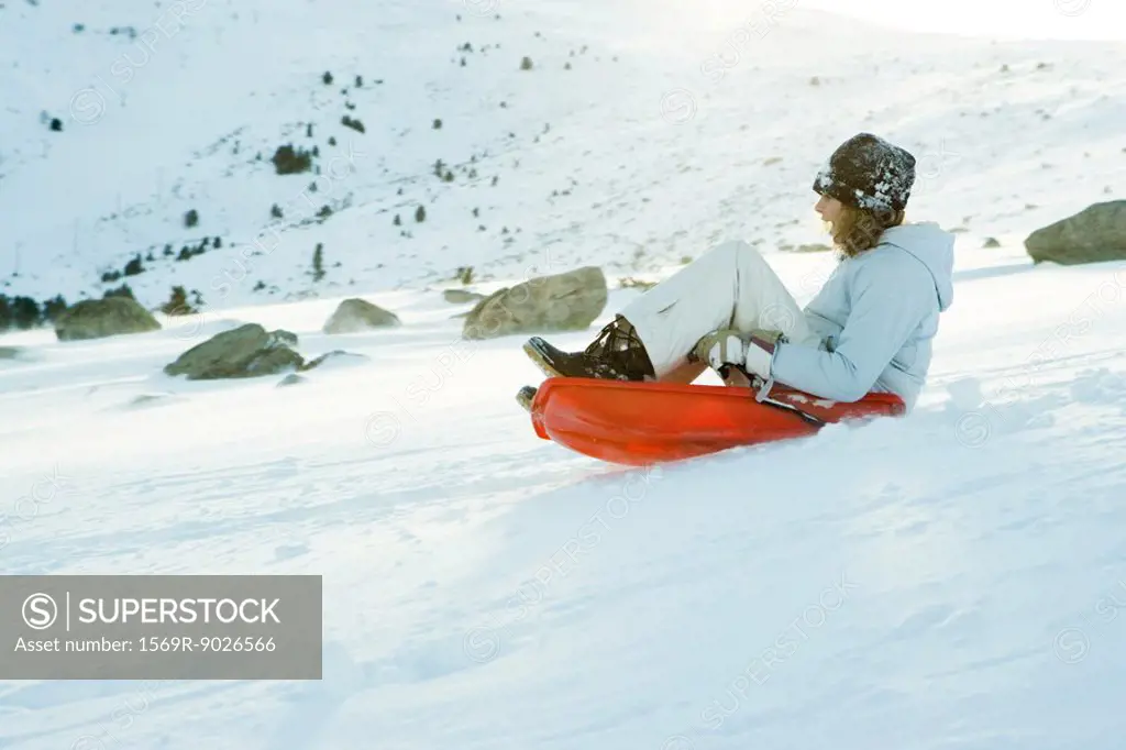 Teenage girl riding sled on ski slope, side view, full length