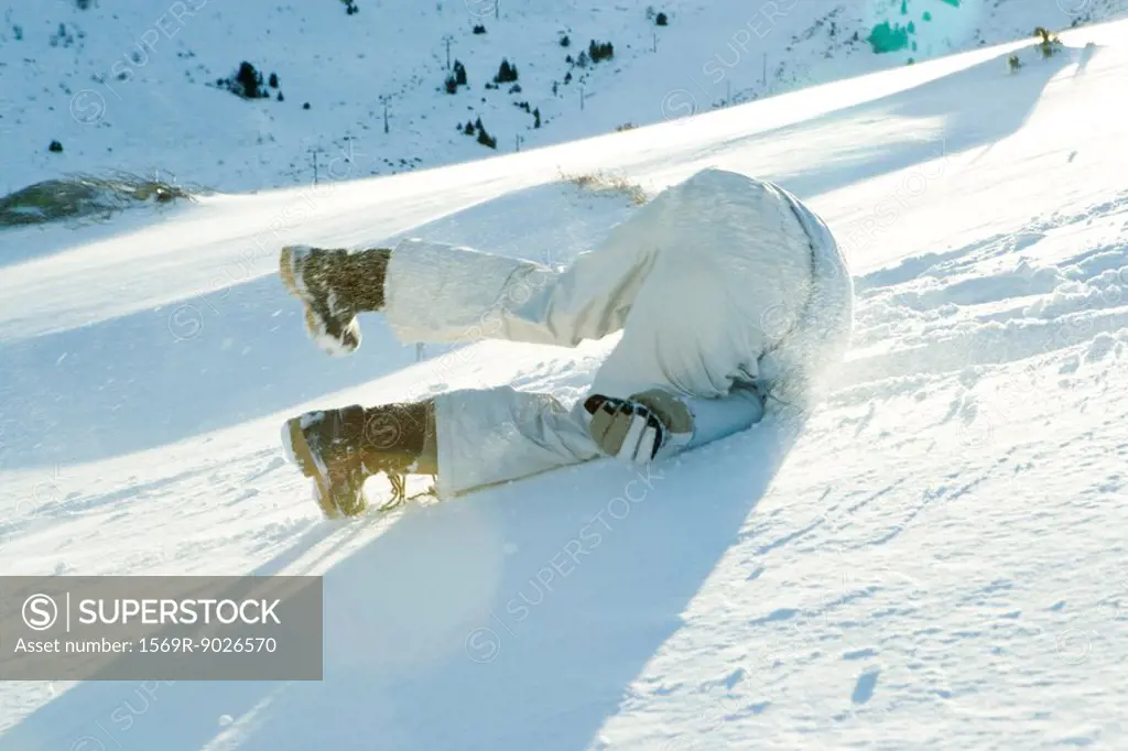 Young skier falling down hill, rear view