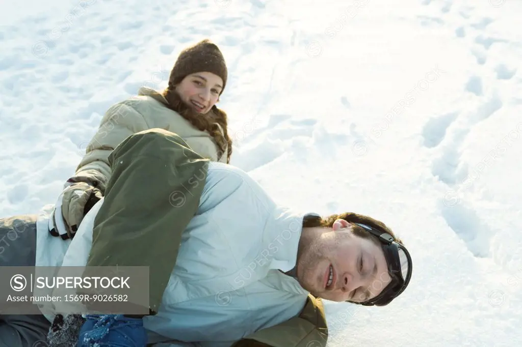 Brother and sister play-fighting in snow, lying in the ground, smiling at camera