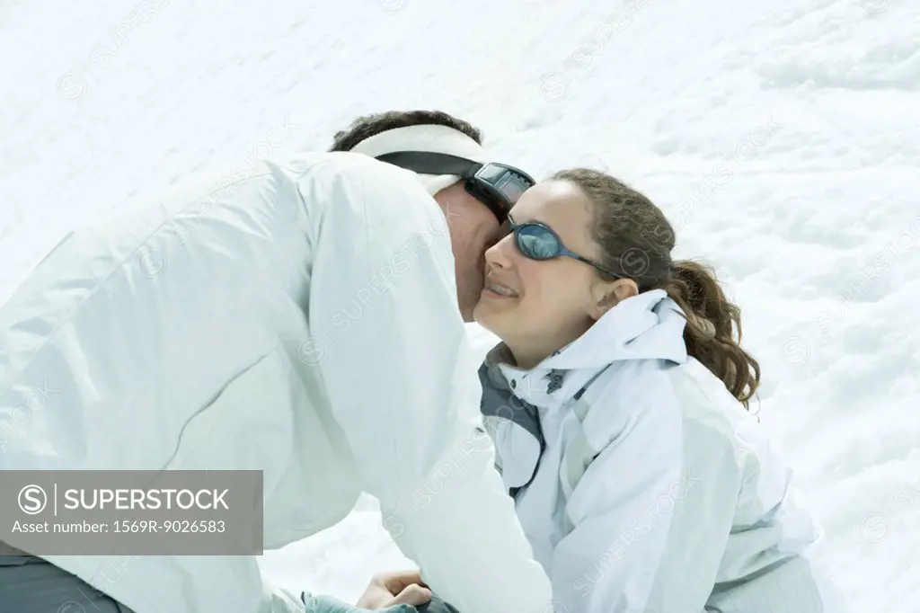Young friends in snow, male whispering in female´s ear, female smiling