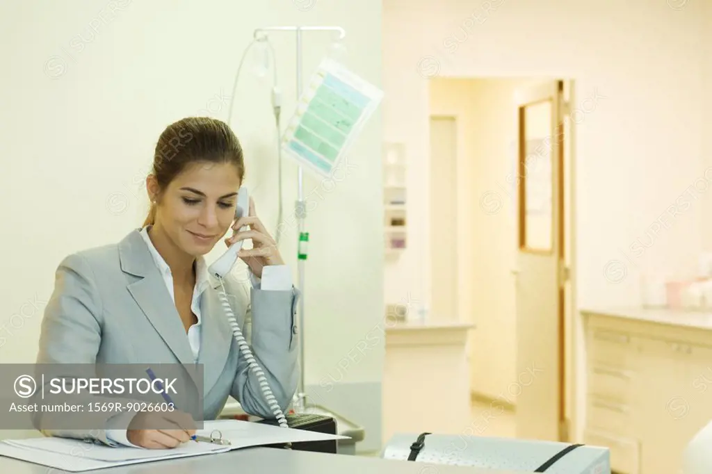 Young woman in doctor´s office, using phone, writing