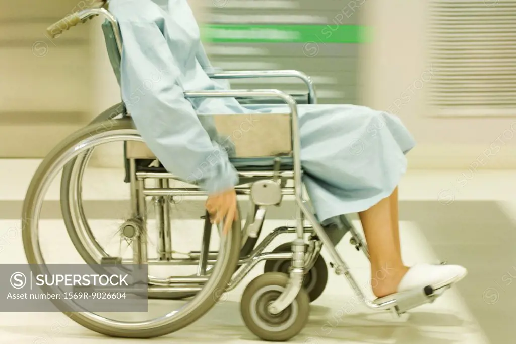 Cropped view of man using wheelchair, dressed in hospital gown, blurred motion