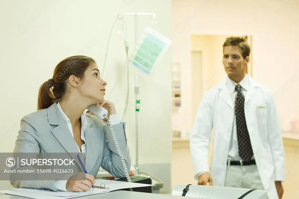 Woman using phone in doctor´s office, looking over shoulder at male doctor