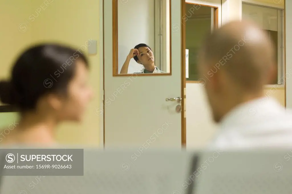 Woman looking at camera through window in hospital waiting room, adults in foreground