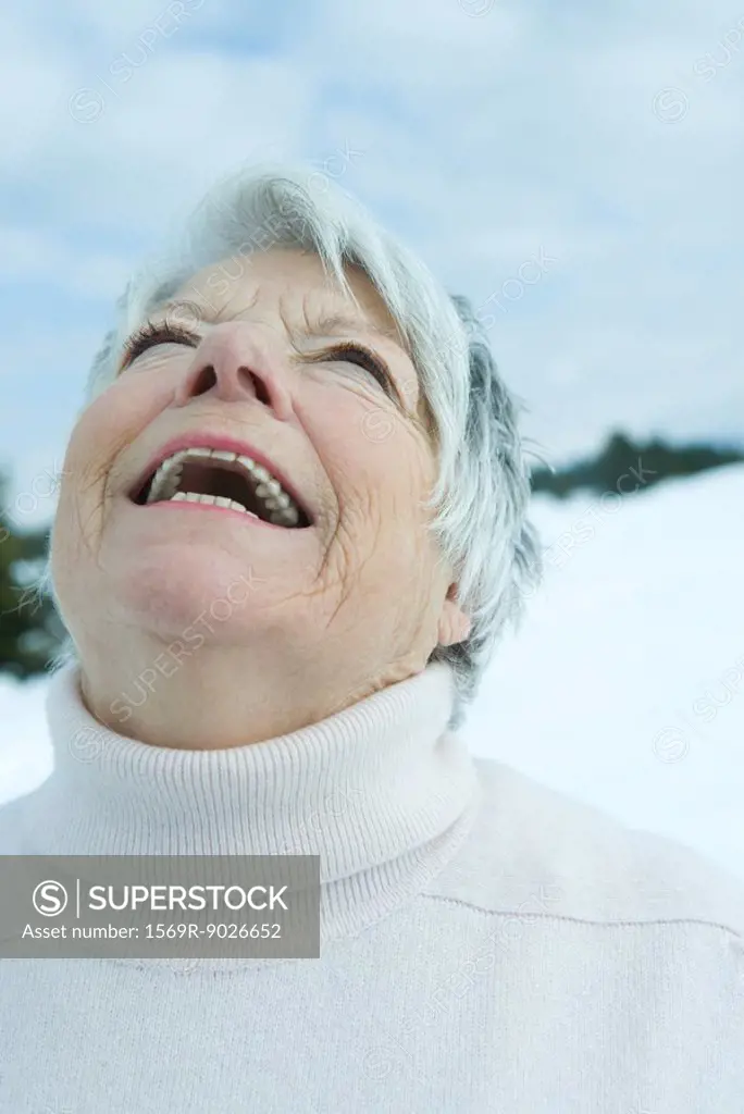 Senior woman laughing with head back in snowy landscape, portrait
