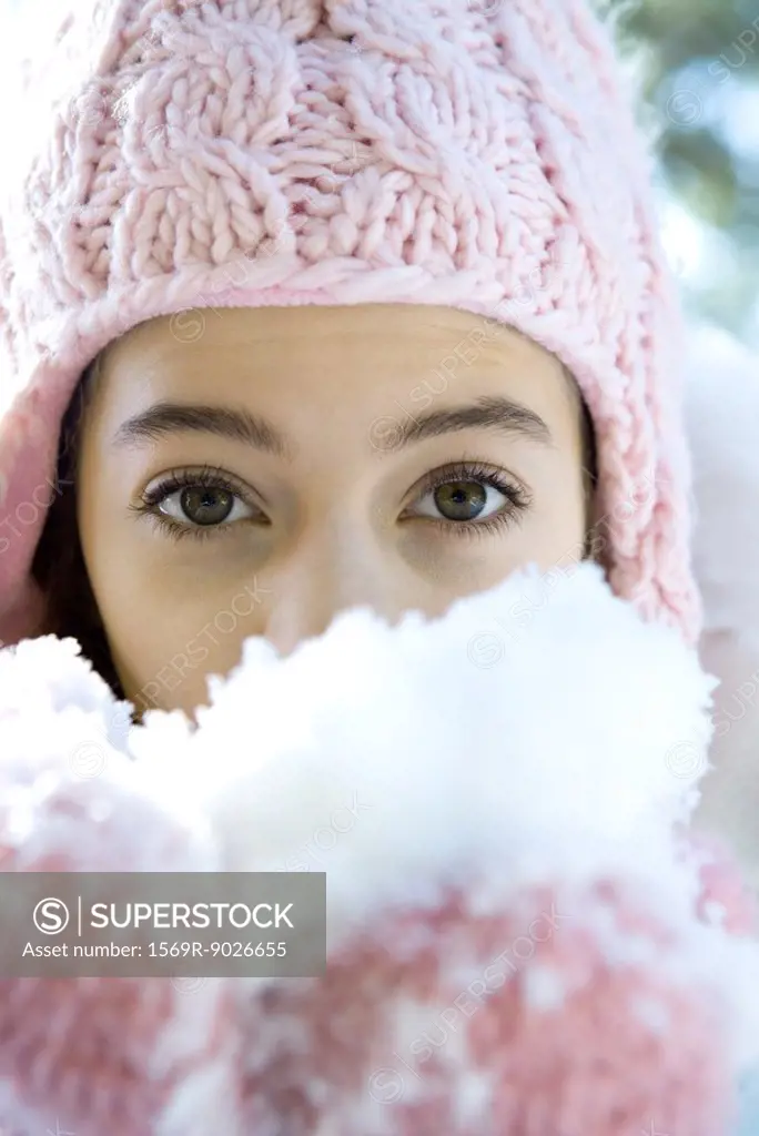 Preteen girl holding handful of snow in mittens, looking at camera
