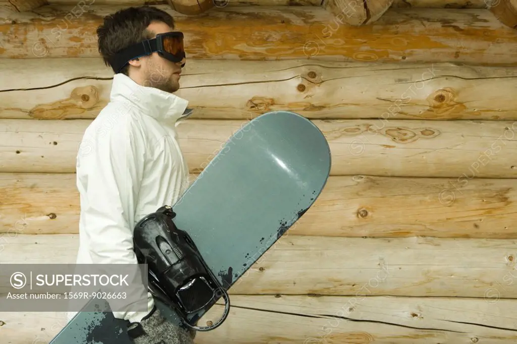 Young man holding snowboard, side view
