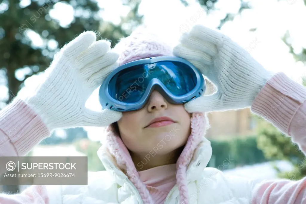Teenage girl adjusting ski goggles, looking up